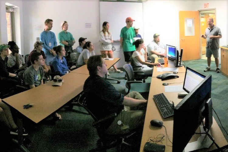 Students from College of Charleston (standing left) with initiative Lead Scientist Peter Etnoyer (standing right) in Charleston’s “pop-up” Exploration Command Center during a NOAA Ship Okeanos Explorer watch party at Hollings Marine Laboratory