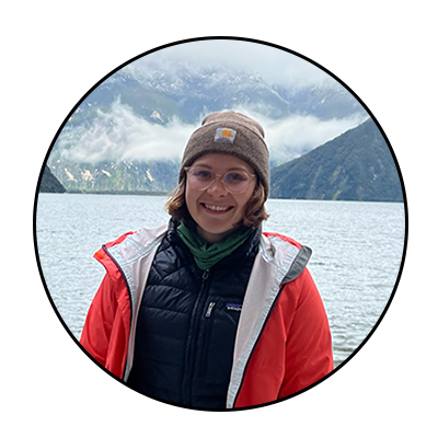 A woman in a brown hat and red jacket smiles in front of fog-covered mountains. Credit: Savannah Goode